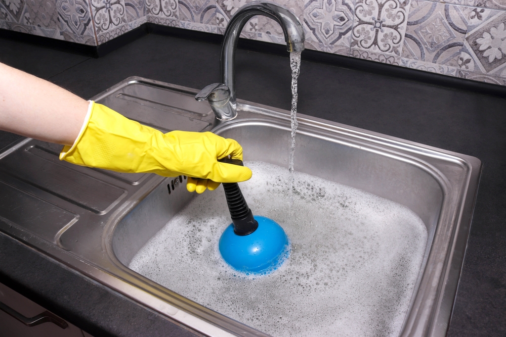 Hand,In,Yellow,Gloves,Cleaning,Sink,With,Plunger.,Overflowing,Kitchen